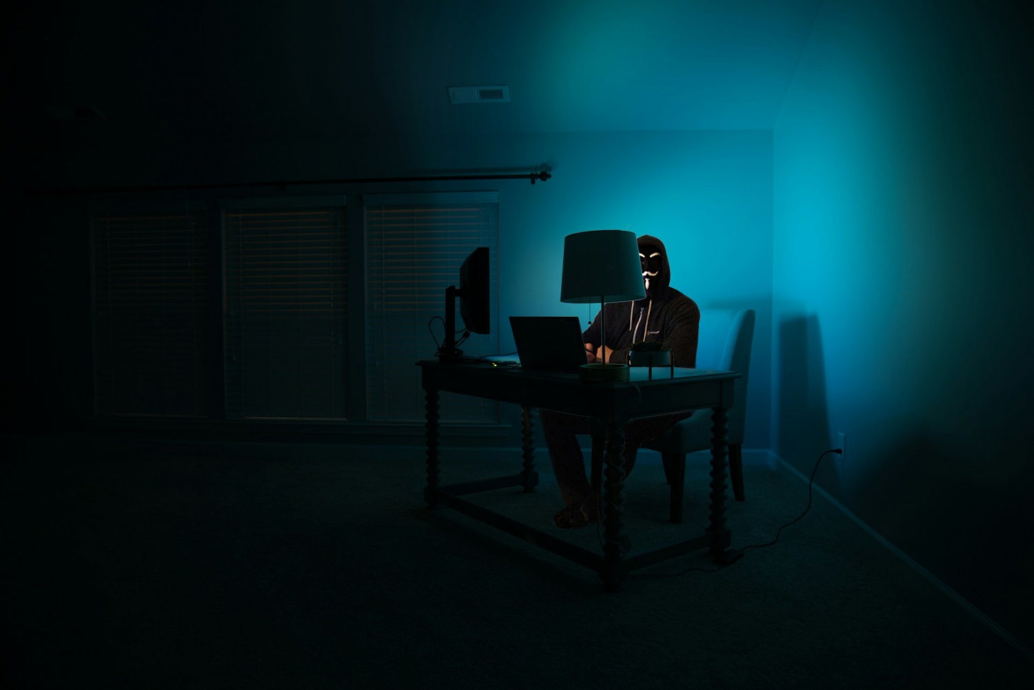 a man at a computer disguised as an anonymous hacker wearing a Guy Fawkes mask.